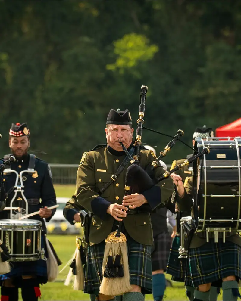 A piper performing with drummers outdoors