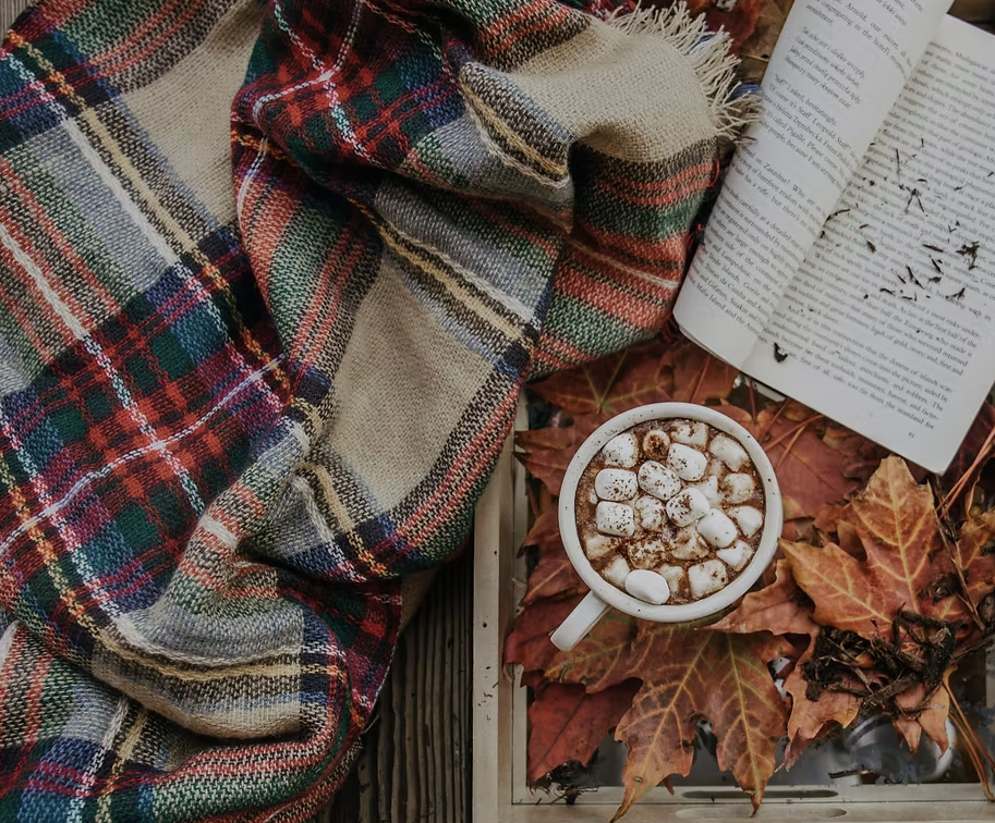 Tartan blanket beside an open book and a mug of hot chocolate
