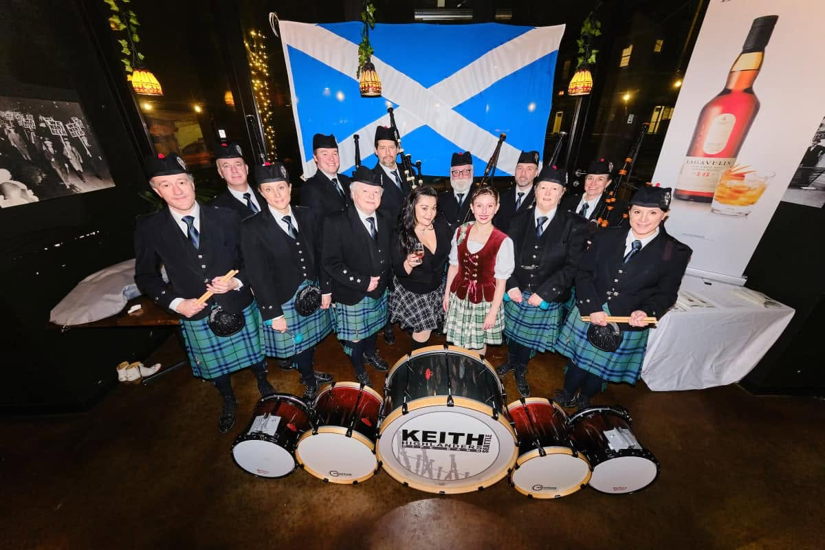Keith Highlanders Pipe Band gathered with its drums in front of a Scottish flag