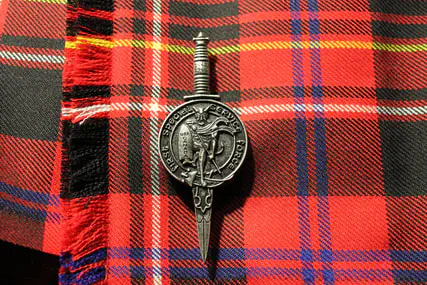The band’s metal kilt pin displayed on red tartan fabric.